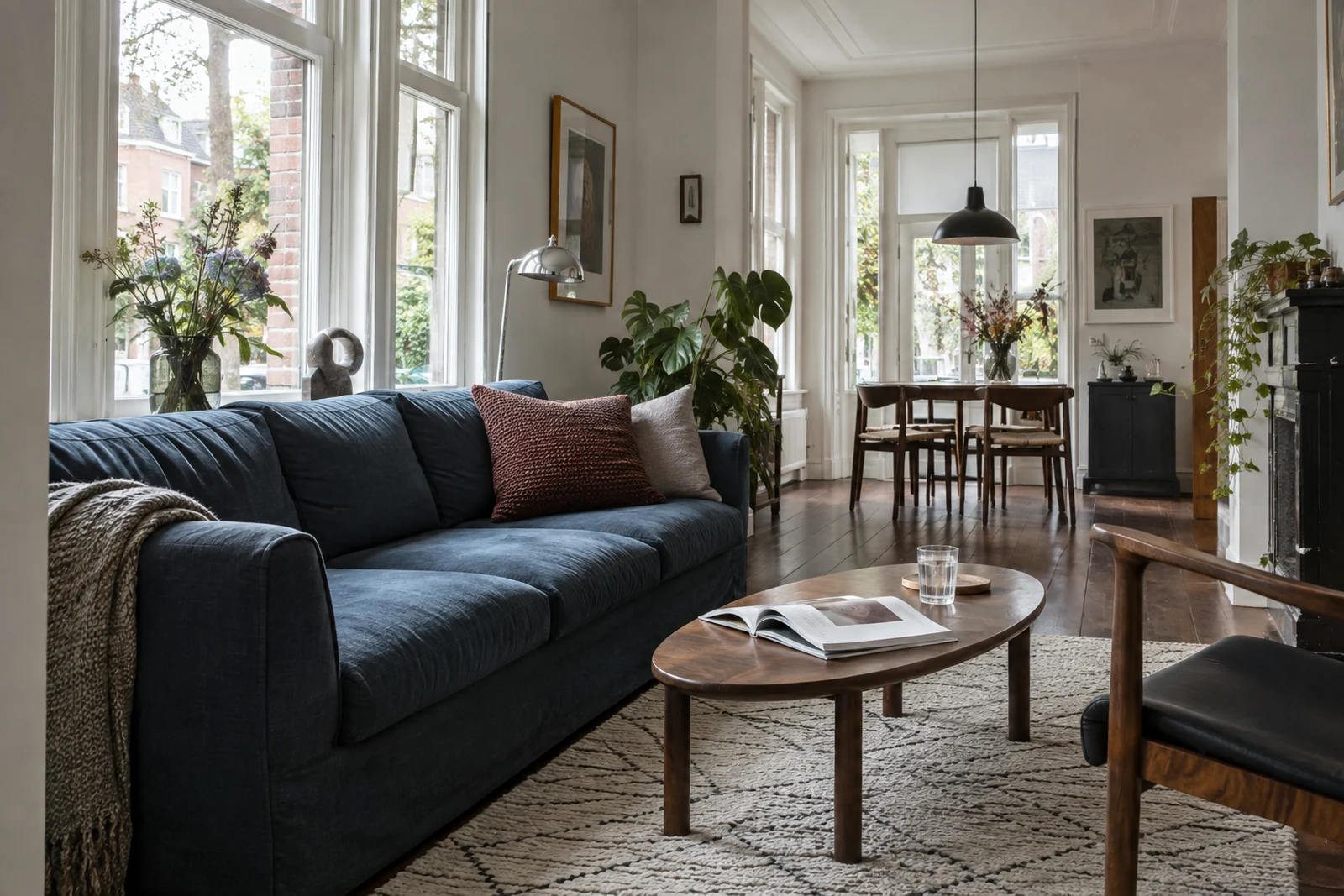 Blauwe stoffen bank en houten salontafel in een lichte woonkamer met een eethoek bij het raam.